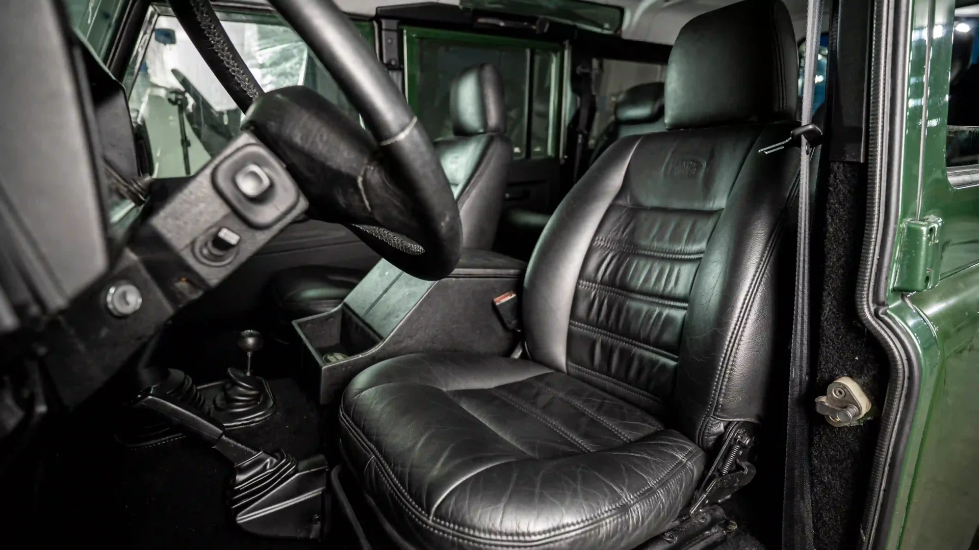 Interior do Land Rover Defender clássico com bancos em couro preto, volante e alavancas de câmbio manual e reduzida 4x4